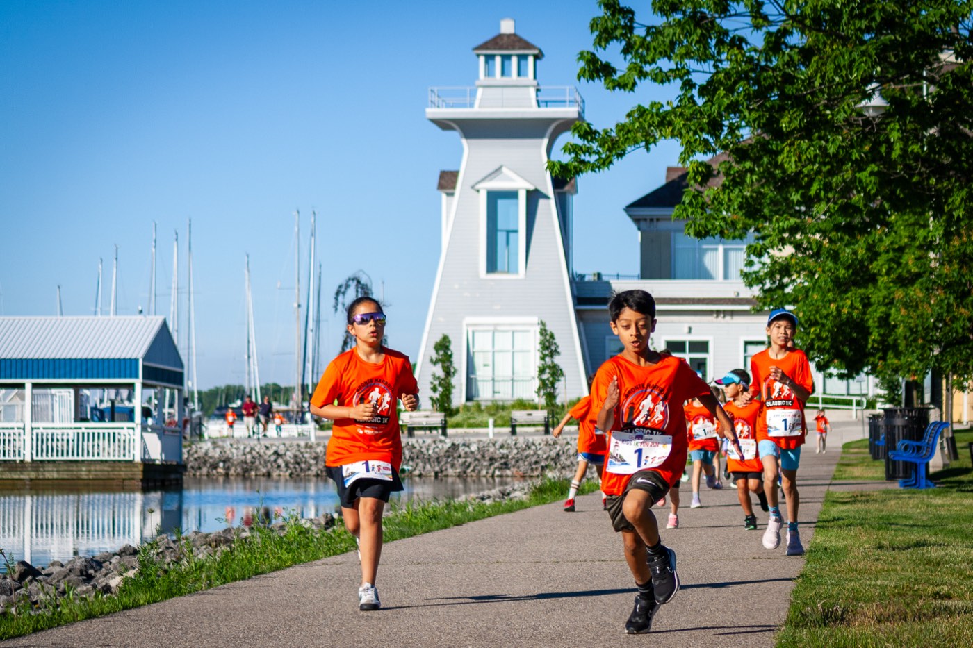 Kids racing past the Bronte lighthouse along the harbour during the Kids 1K at the Mercedes-Benz Oakville Bronte Harbour Classic, June 21, 2026