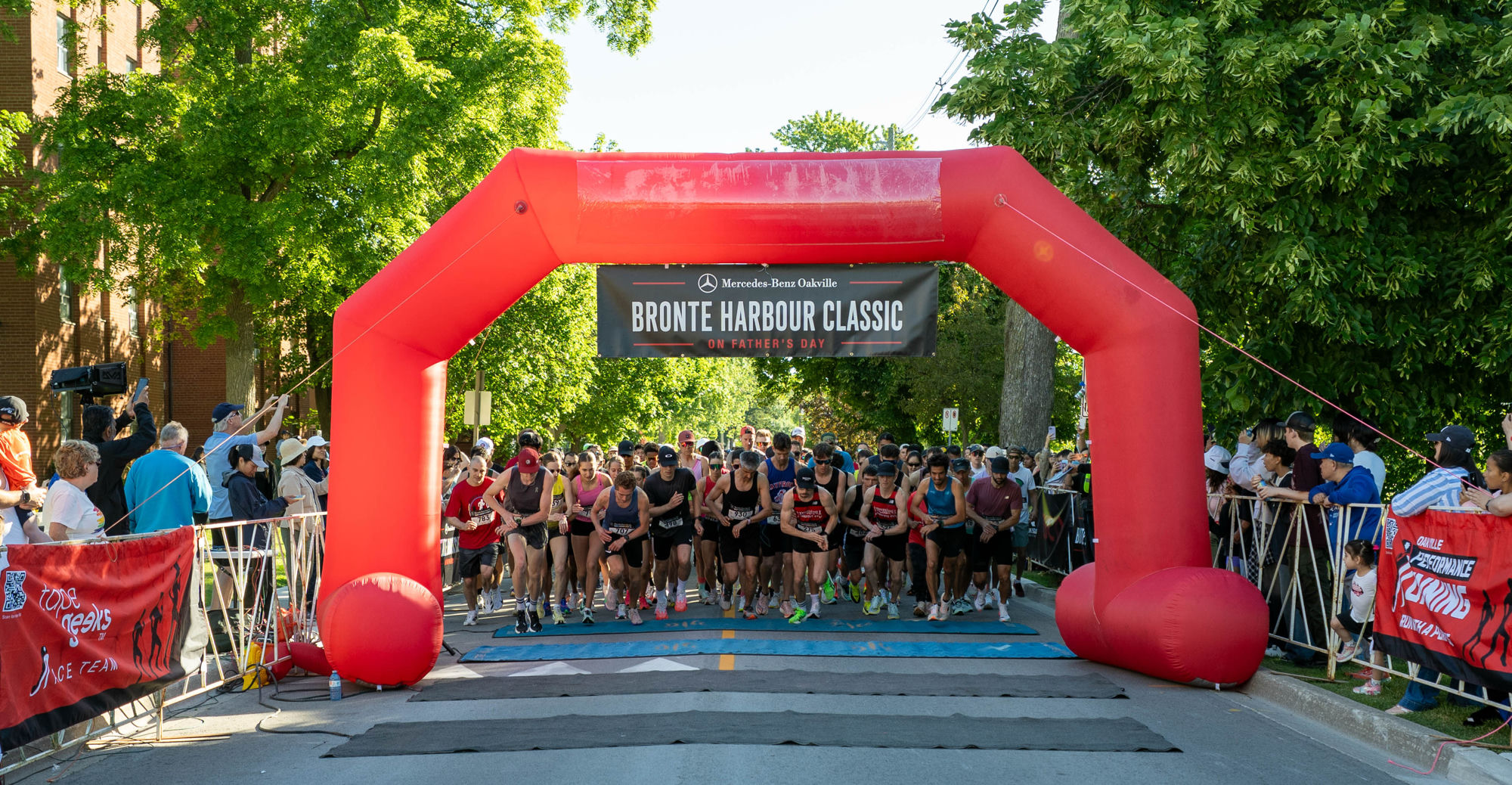 800+ runners launch under the red Mercedes-Benz Oakville arch at the start of the inaugural Bronte Harbour Classic 5K, Bronte Heritage Waterfront Park, Father's Day, June 21, 2026